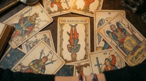 An overhead shot of vintage tarot cards spread across a wooden table, with "THE HANGED MAN" featured prominently in the center.